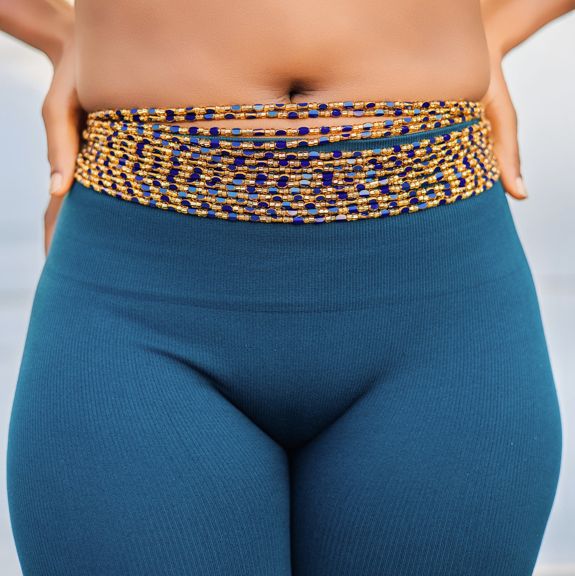 Person wearing Achalugo Wild Iris blue and gold waistbeads against a neutral background.